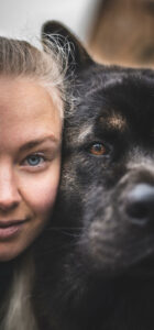 Half of a woman's face with shaved hair and blue eyes next to half of a dog's face