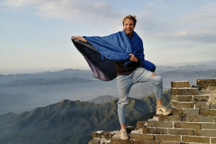 Oliver steht auf einer Mauer auf einem Berggipfel, hinter ihm weitere wolkenverhangene Berggipfel