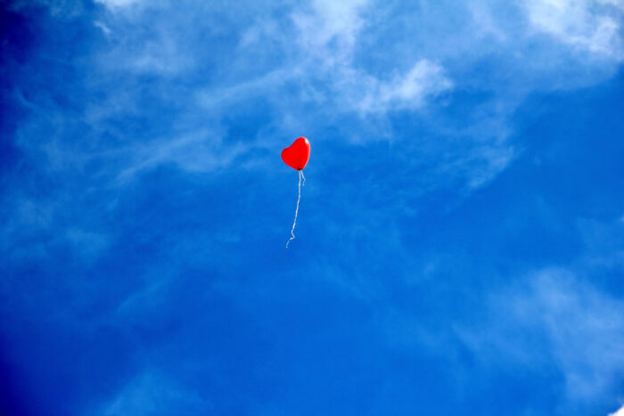 Kleiner roter Herzluftballon fliegt über weiten blauen Himmel